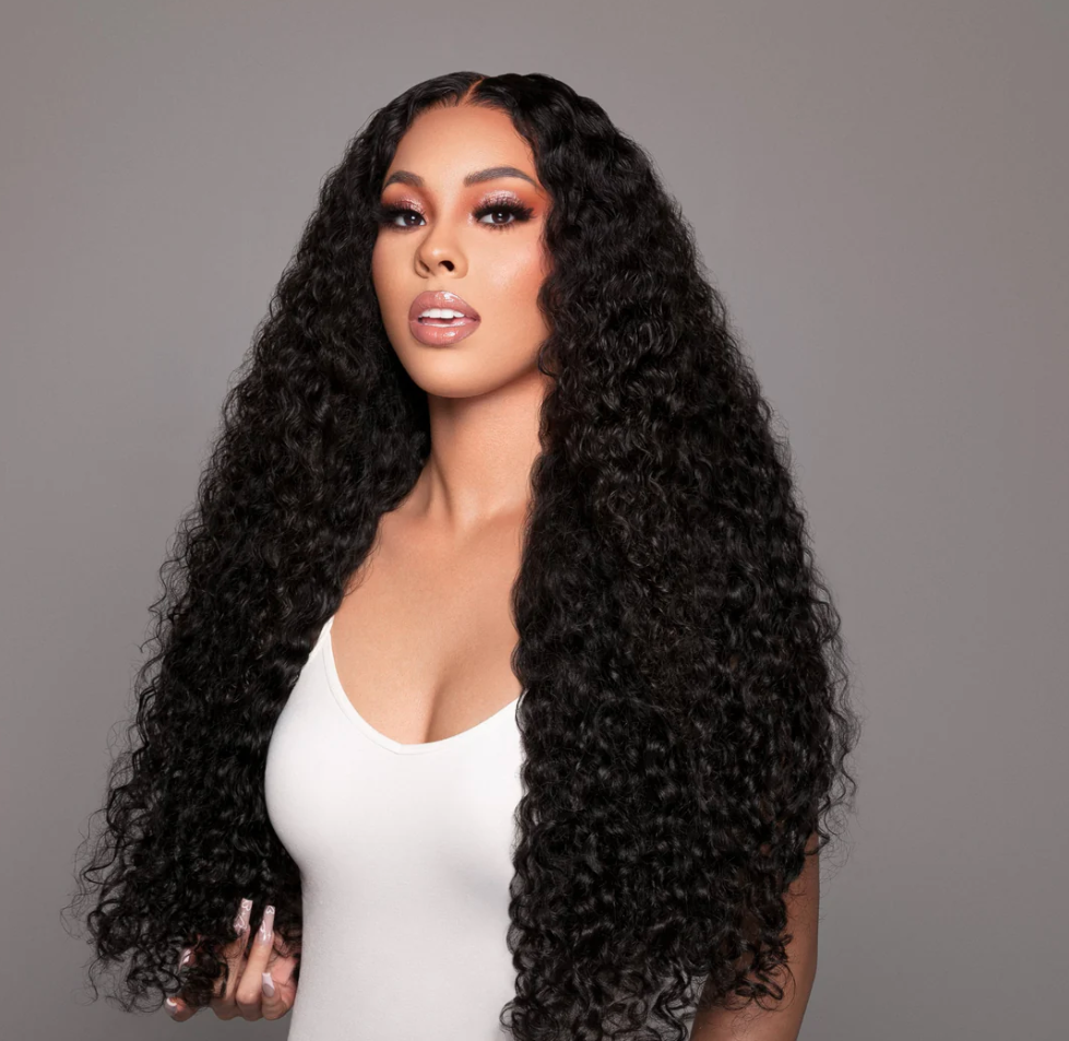 Woman with long, curly black hair wearing a white top against a gray background