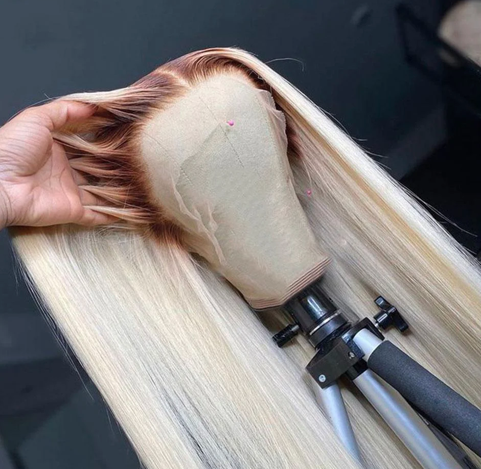 Blonde wig on a mannequin head with a tripod supporting it against a dark background