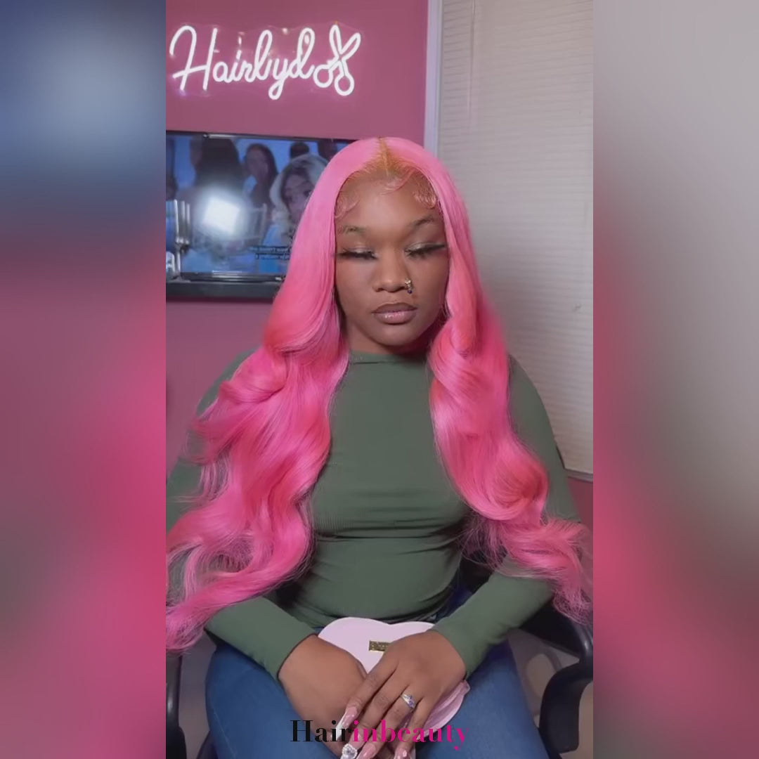 A woman sitting in a salon chair wearing a pink wig smiling 