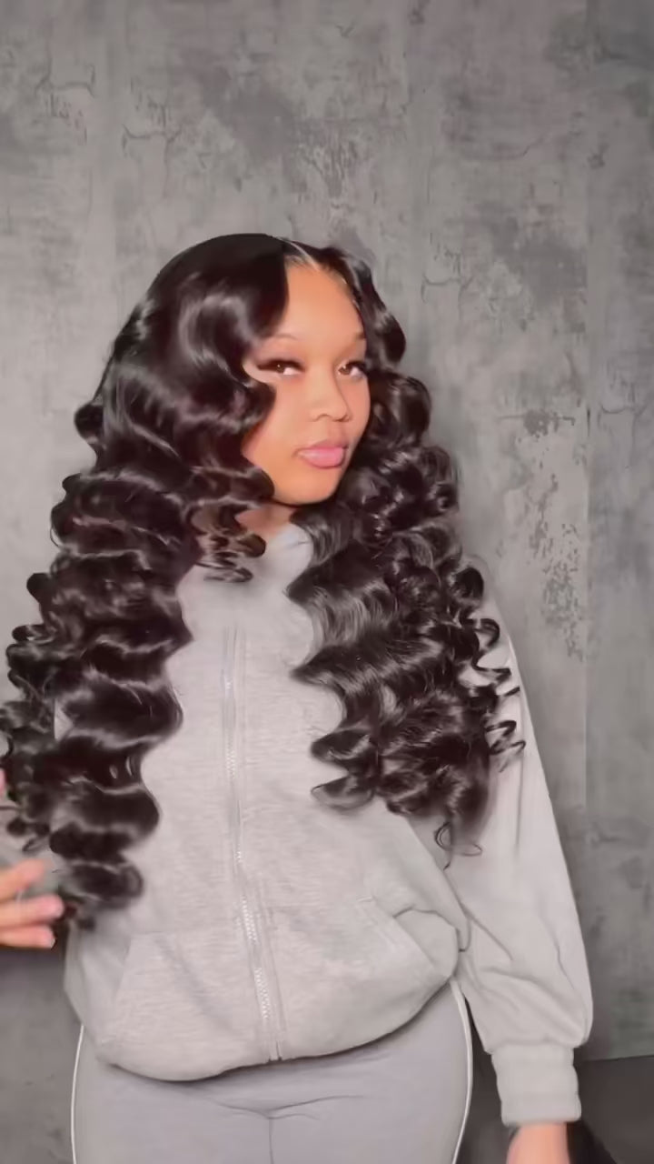 Woman with voluminous black hair styled in waves, wearing a grey outfit.